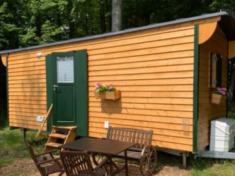 Hébergement glamping Ferienhof Jeiler - Pipowagen Noordrijn Westfalen avec façade en bois et coin repas extérieur.