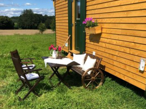 Espace détente extérieur avec fleurs, table, chaises et cabane de bois chez Ferienhof Jeiler glamping.