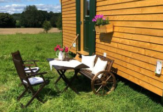 Gemütlicher Sitzbereich im Freien am Pipowagen mit Blumen und Aussicht, Ferienhof Jeiler, Nordrhein-Westfalen.