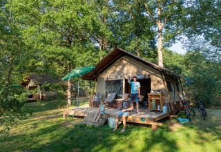 Familie foran glamping-telt på Camping Huttopia De Roos i Overijssel, omgivet af træer og natur.
