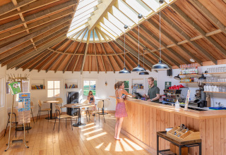 Vista interior de la recepción y cafetería de Camping Huttopia De Roos con suelos y techo de madera.