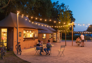 Espace extérieur du Camping Huttopia De Roos avec guirlandes lumineuses et clients en soirée glamping.