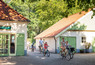 Menschen fahren Fahrrad durch das Campinggelände von Huttopia De Roos mit roten Dächern in Overijssel.