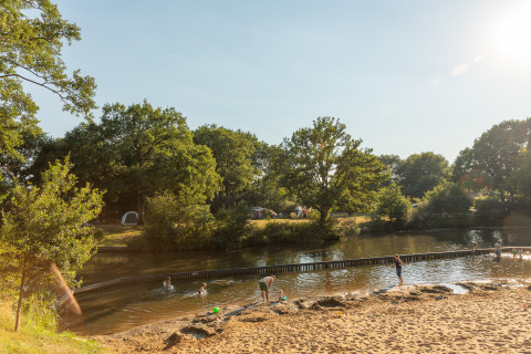 Børn leger ved sandstrand og flod i skovområde på Camping Huttopia De Roos i Overijssel, Holland.