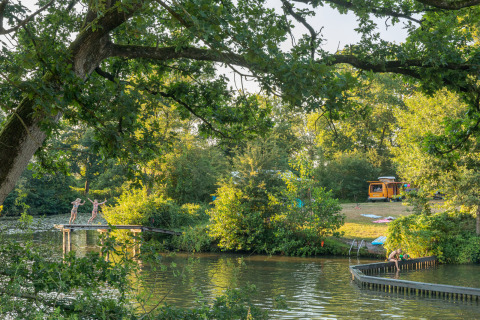Bambini giocano sul fiume al Camping Huttopia De Roos in Overijssel, con camper e natura sullo sfondo.