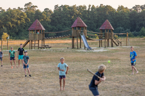 Børn leger baseball foran en legeplads på Camping Huttopia De Roos i naturskønne Overijssel, Holland.