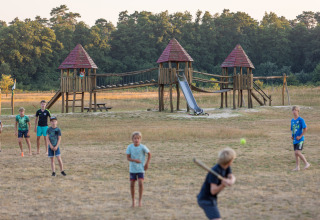 Niños jugando béisbol junto a un parque infantil en Camping Huttopia De Roos, Overijssel, Países Bajos.