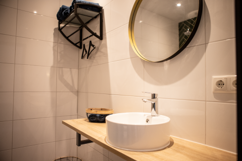 Modernes Badezimmer mit rundem Spiegel, Waschbecken und hellen Fliesen in Landgoed Lindehof – Natuur Lodges Friesland.