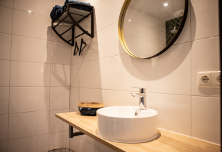 Baño moderno con azulejos blancos, espejo redondo y lavabo en Landgoed Lindehof – Natuur Lodges Friesland glamping.