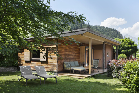 Gemütliche Holzhütte mit Terrasse und Gartenmöbeln, eingebettet im Grünen vor Tiroler Bergkulisse.