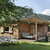 Cozy wooden glamping lodge with a porch and outdoor seating, surrounded by greenery and mountain views.