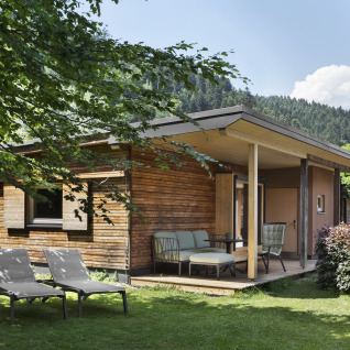 Knusse houten tuinlodge met veranda en tuinmeubels, omgeven door groen en bergen in Tirol.