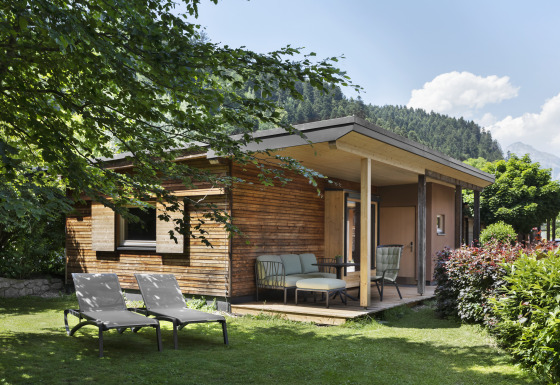 Gemütliche Holzhütte mit Terrasse und Gartenmöbeln, eingebettet im Grünen vor Tiroler Bergkulisse.
