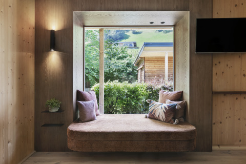 Moderne Glamping-Unterkunft in Tirol mit gemütlicher Fensternische, Kissen und Blick ins Grüne.