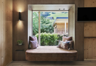 Moderne Glamping-Unterkunft in Tirol mit gemütlicher Fensternische, Kissen und Blick ins Grüne.