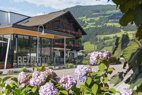 Natürlich Hell Camping & Aparthotel - Tuin Lodges Tirol con flores, recepción y montañas verdes al fondo.