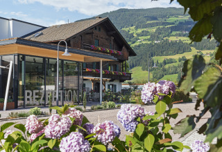 Natürlich Hell Camping & Aparthotel - Tuin Lodges Tirol with blooming flowers, reception, and scenic green hills.