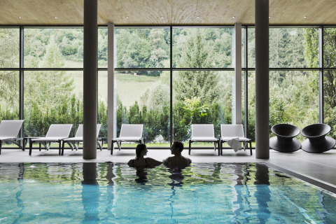 Piscina interna con due persone, lettini prendisole e vista sul bosco presso Natürlich Hell Camping & Aparthotel - Tuin Lodges Tirol.