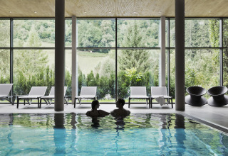 Piscina cubierta con dos personas, tumbonas y vistas al bosque en Natürlich Hell Camping & Aparthotel - Tuin Lodges Tirol.