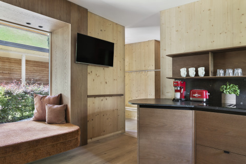 Modern glamping lodge with wood interiors, flat-screen TV, window bench, and coffee maker at Natürlich Hell.
