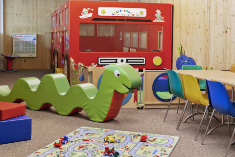 Sala de juegos colorida con juguete de serpiente, autobús y sillas en Natürlich Hell Camping & Aparthotel - Tuin Lodges Tirol.
