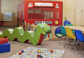 Colorful indoor playroom with green snake toy, bus structure, and chairs at Natürlich Hell Camping & Aparthotel - Tuin Lodges Tirol.