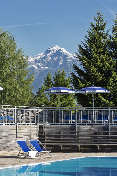 Piscina con sdraio e ombrelloni blu, vista montagna e alberi al Natürlich Hell Camping Tirol.