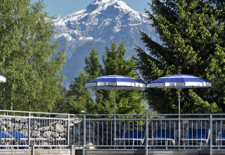 Poolside with blue loungers, umbrellas, wooden deck, mountain and trees at Natürlich Hell Camping Tirol.