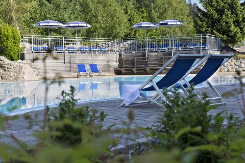 Buitenzwembad met blauwe ligstoelen en parasols bij Natürlich Hell Camping & Aparthotel - Tuin Lodges Tirol.