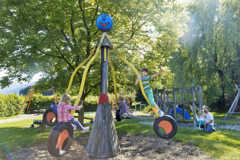 Niños jugando en un parque infantil con columpios de neumáticos en Natürlich Hell Camping & Aparthotel - Tuin Lodges Tirol.