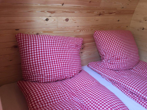 Twee bedden met rood-wit geruite dekbedden en kussens in een luxe houten pod op Camping Hegne.