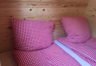 Deux lits avec couettes et oreillers à carreaux rouges et blancs dans un pod de luxe en bois au Camping Hegne.
