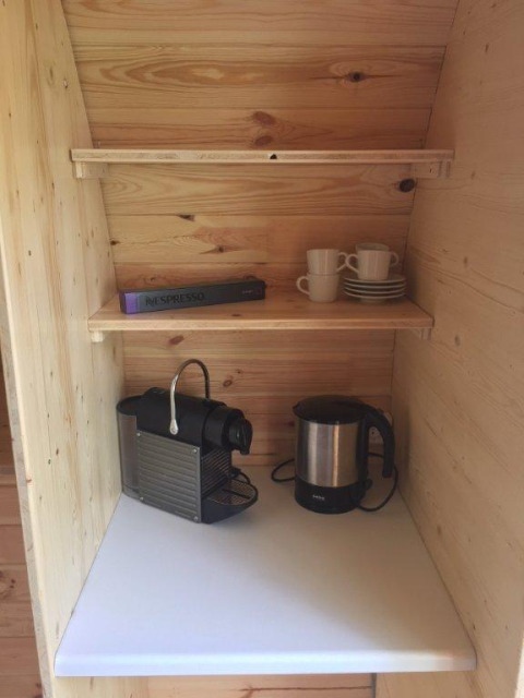 Pod de luxe Camping Hegne Bodensee : étagères bois, machine à café, bouilloire et tasses.