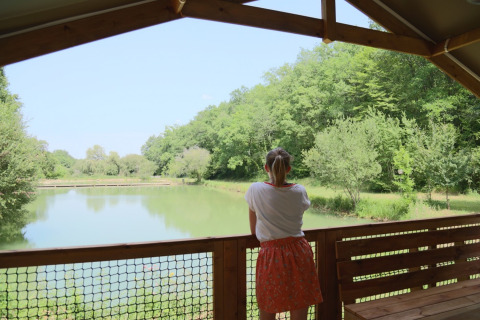 Femme sur la terrasse d’un hébergement glamping face à un lac, Les Truffières de Dordogne, Nouvelle-Aquitaine.