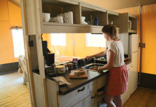 Woman washing dishes in a modern kitchen at glamping site Les Truffières de Dordogne – La Bouquerie – Safaritenten Nouvelle-Aquitaine.