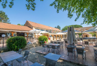 Außenterrasse mit Tischen und Sonnenschirmen bei Les Truffières de Dordogne – La Bouquerie Safarizelten.