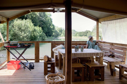 Holzterrasse der Glamping-Unterkunft Les Truffières de Dordogne mit Blick auf Fluss und grüne Bäume.