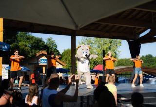 Stage entertainment with performers in orange shirts and a bear mascot at Les Truffières de Dordogne – La Bouquerie – Safaritenten.