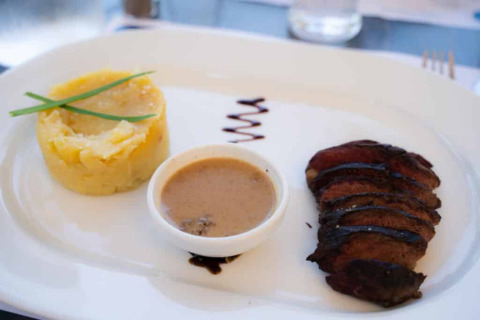 Feines Abendessen mit Kartoffelpüree, gegrilltem Fleisch, Soße und Dekoration auf einem weißen Teller.