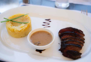 Feines Abendessen mit Kartoffelpüree, gegrilltem Fleisch, Soße und Dekoration auf einem weißen Teller.