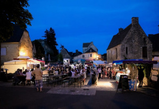 Atmosfera serale a Les Truffières de Dordogne – La Bouquerie glamping con bancarelle e persone sedute.