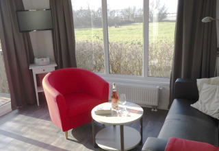 Indvendigt i en moderne chalet på Camping Wackerballig, med udsigt til grønne marker og komfortabel stue.