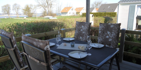 Buiteneethoek met gedekte tafel en vier stoelen op terras, uitkijkend op grasveld en vakantiewoningen.