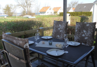Zona pranzo esterna con tavolo apparecchiato e quattro sedie su terrazza, vista su prato e chalet sullo sfondo.