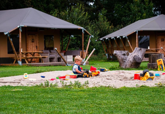 Een kind speelt in de zandbak met speelgoed voor de lodgetenten op Glamping de Bosweide in Noord-Brabant.