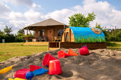 Hébergement glamping en Brabant-Septentrional avec bac à sable et jouets, devant une tente lodge de luxe.