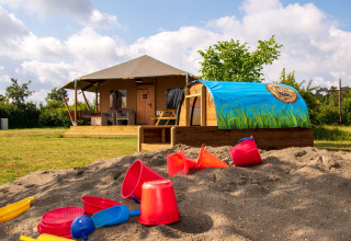 Hébergement glamping en Brabant-Septentrional avec bac à sable et jouets, devant une tente lodge de luxe.