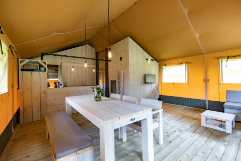 Binnenaanzicht van luxe glamping lodgetent in Noord-Brabant met eettafel en sfeervolle inrichting.