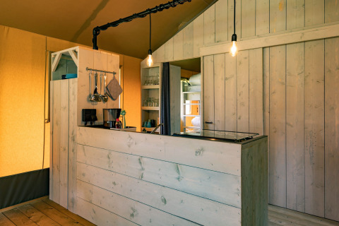 Interieur van lodgetent bij Glamping de Bosweide met houten panelen, keuken en sfeervolle verlichting.