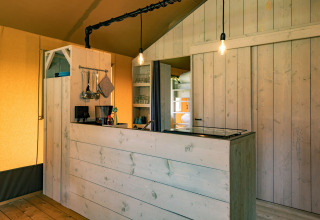 Interiør af Glamping de Bosweide lodgetelt med træpaneler, køkkenfaciliteter og hyggelig atmosfære.